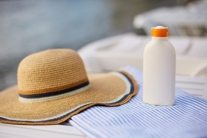 Suntan cream bottle on beach towel with sea shore on background. Sunscreen on deck chair outdoors on sunrise or sunset at luxury spa resort. Skin care and protection concept and travel. Golden tan.
