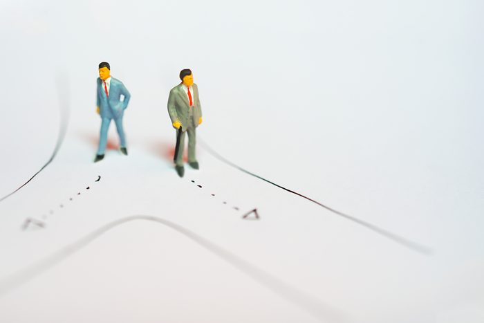 Miniature figures of Two business man standing on road selecting way to walk as decision making on white notebook paper drawing line with copyspace - business success backgroun concept