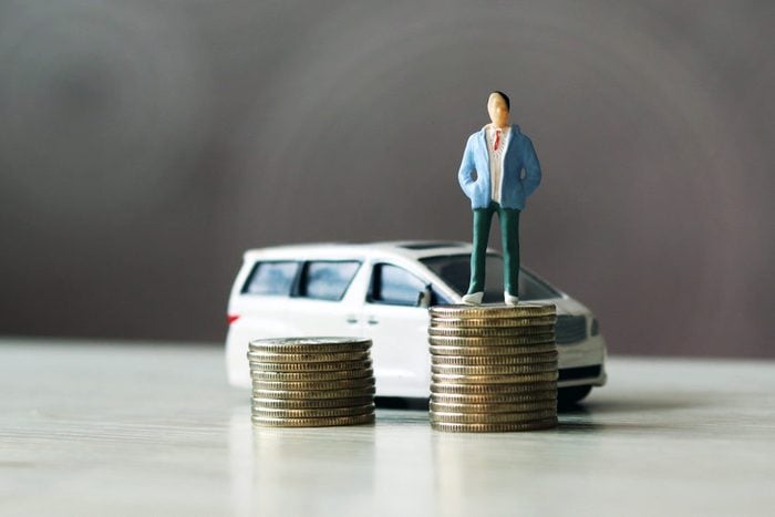 miniature people. The man standing on top of the coins and the car behind them. 