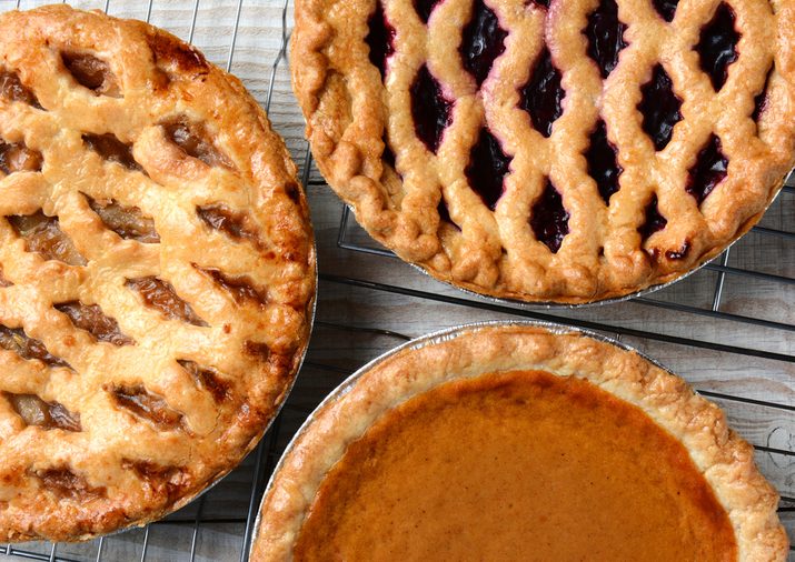 Three pies on cooling racks. High angle closeup shot of fresh baked apple, cherry and pumpkin pastries on wire racks on a rustic wood kitchen table. Horizontal format.