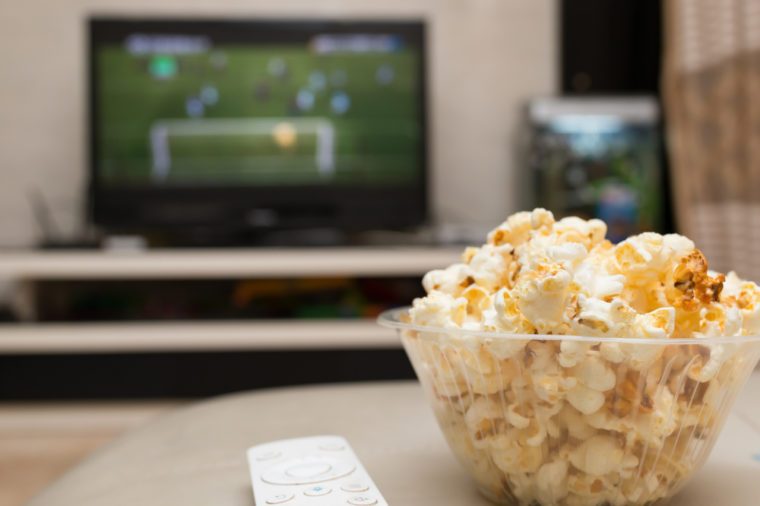 popcorn and remote control on sofa with a TV broadcasting soccer match on background