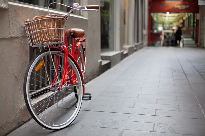A shoppers red commuting bicycle with basket is parked in a lane-way in Melbourne, Australia, with shops in the background.