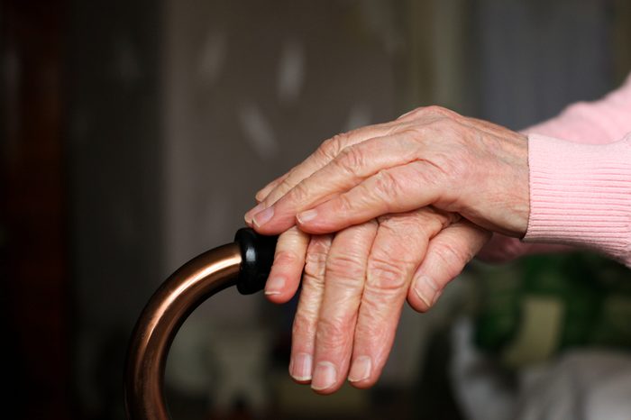 Elderly woman holds walking cane in her room. Senior lady experiencing bad service and conditions in retirement nursing home. Close up of mature woman's wrinkled hands laying on stick. Aging concept.