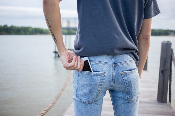 Close up on young man with authentic tattoos on arm taking out smartphone with protective glass out of his skinny jeans pocket