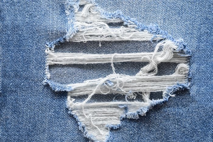 Jeans in wash blue with rip. Denim background, texture. Ripped destructed detail, close up.
