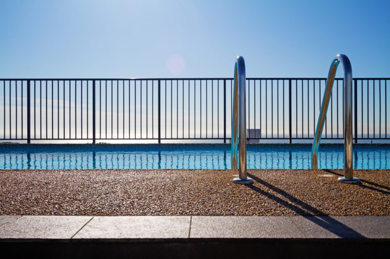 Swimming pool edge with ladder, fence and sky background