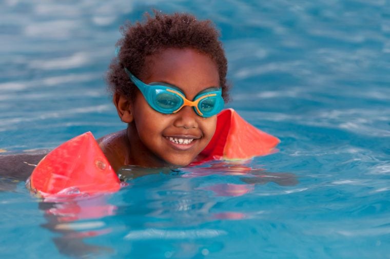 Little african child with orange sleeve floats in the pool 