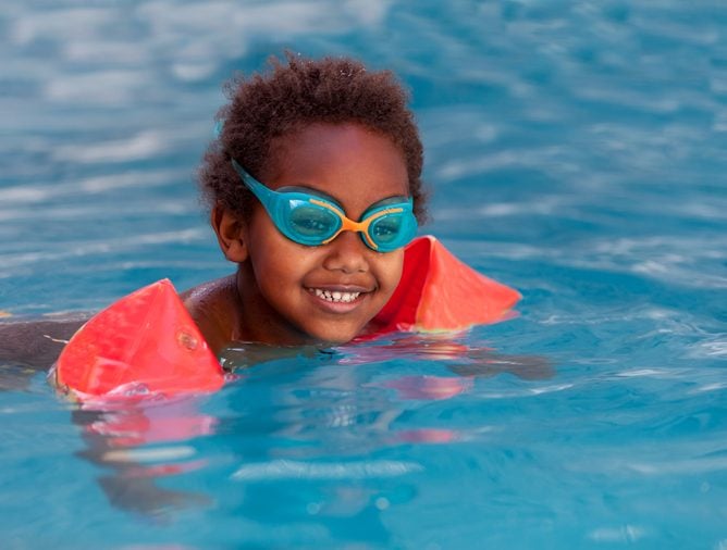 Little african child with orange sleeve floats in the pool 