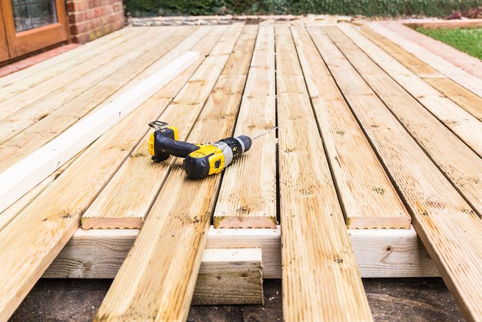 A new wooden, timber deck being constructed. it is partially completed. a drill can be seen on the decking.