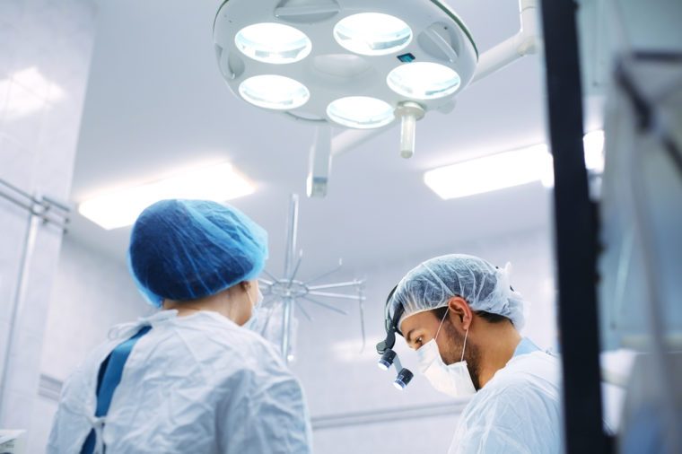Breast augmentation, enlargement, enhancement. Surgeon and his assistant performing cosmetic surgery in hospital operating room. In mask wearing during medical procedure