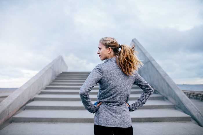 Outdoor shot of young woman standing by a stairs and looking away. Fitness female before a run.