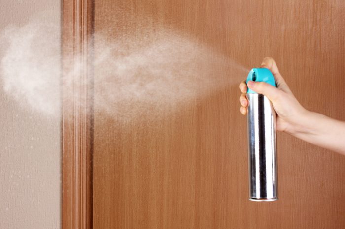 Sprayed air freshener in hand on room background