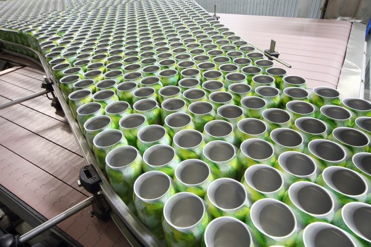 Many open green cans for drinks move on conveyor at large modern factory.