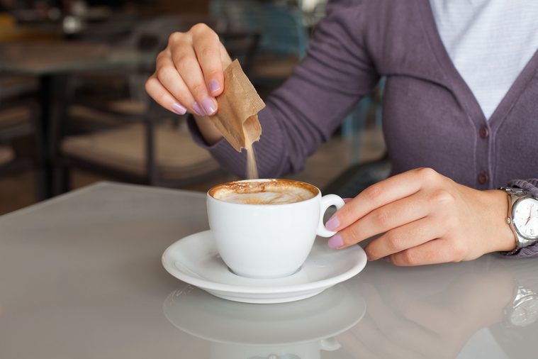 Young woman adding sugar to the coffee