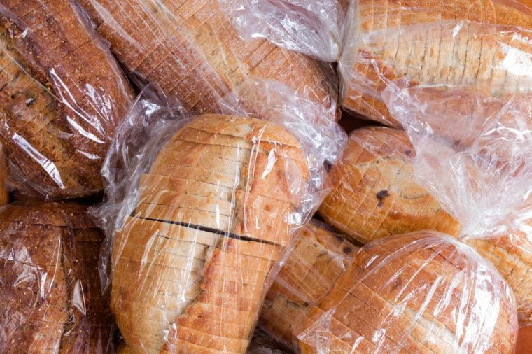 Plastic bags of assorted varieties of fresh sliced bread for a food drive piled on top of one another in a full frame background view
