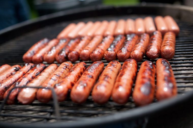 Several cooking hot dogs on a grill
