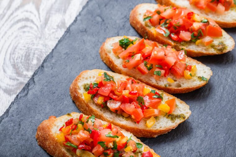 Appetizer bruschetta with chopped vegetables on ciabatta bread on stone slate background close up. Delicious snacks, sandwiches, crostini, canape, antipasti on party or picnic time. Top view
