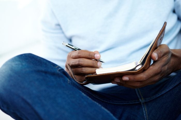 Hands of young African man writing something in notepad