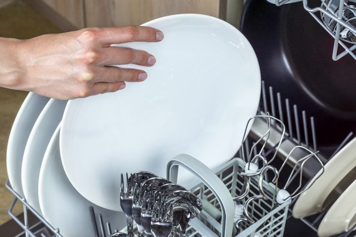Unloading clean dishes from the dishwasher machine. Focus on hands.