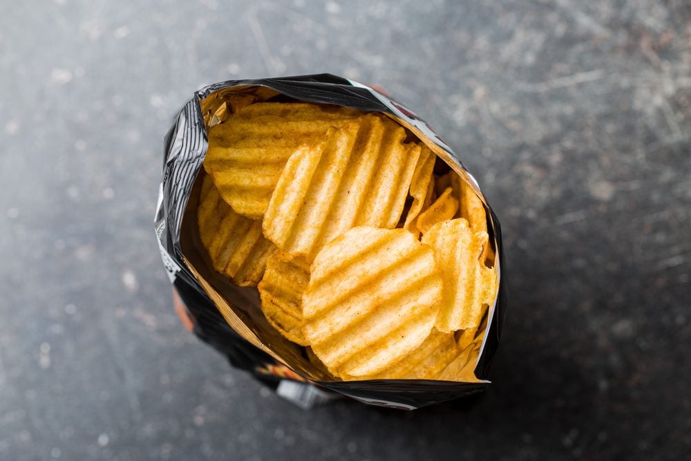 Crinkle cut potato chips on kitchen table. Tasty spicy potato chips in bag. Top view.