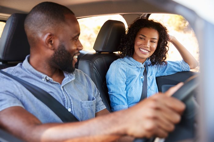 Young black couple in car on road trip smiling at each other
