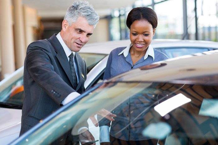 friendly mature car dealer showing new car to african customer