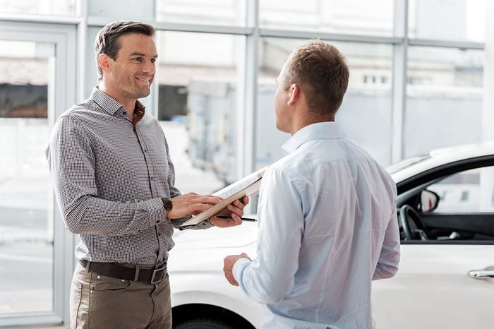Outgoing man telling with worker in car dealership