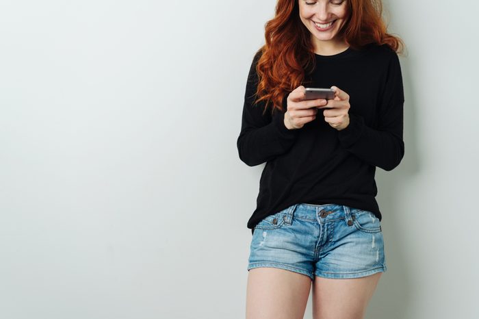 Pretty smiling young woman reading an sms or text message on her mobile phone with a smile in a close up cropped view
