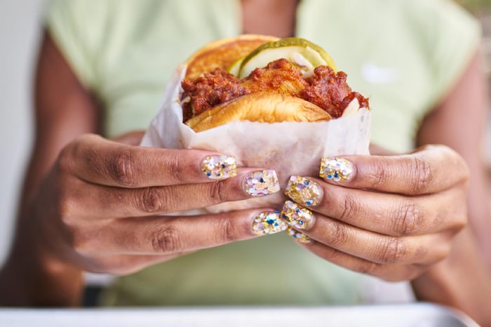close up of woman with pretty nails holding fried spicy chicken sandwich