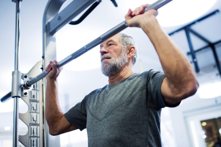 Senior man in gym doing pull-ups on horizontal bar.