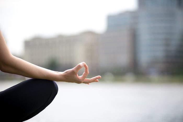 Meditation concept. Close up of hands of young office yogi woman sitting cross legged in yoga Easy Sukhasana Pose on riverbank in the city, meditating with fingers in Jnana mudra