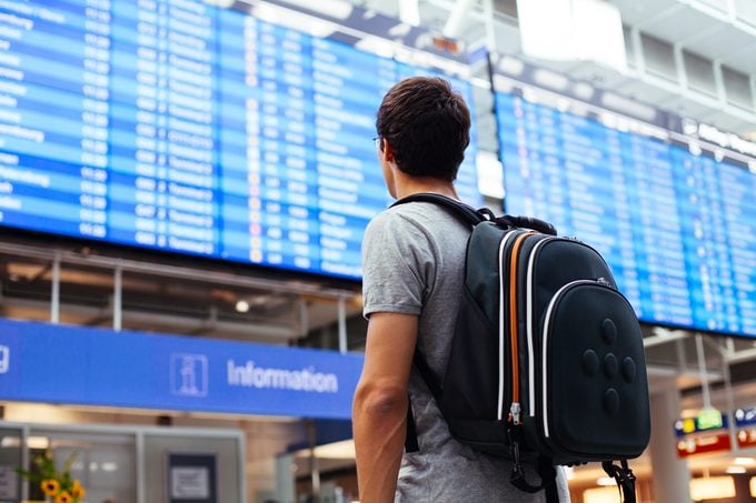 Young man with backpack in airport near flight timetable