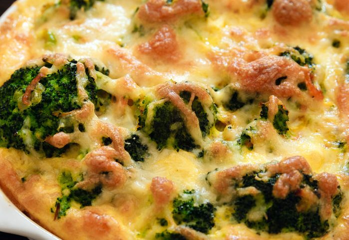 Broccoli baked with cheese and egg, lined in a white dish on a wooden table