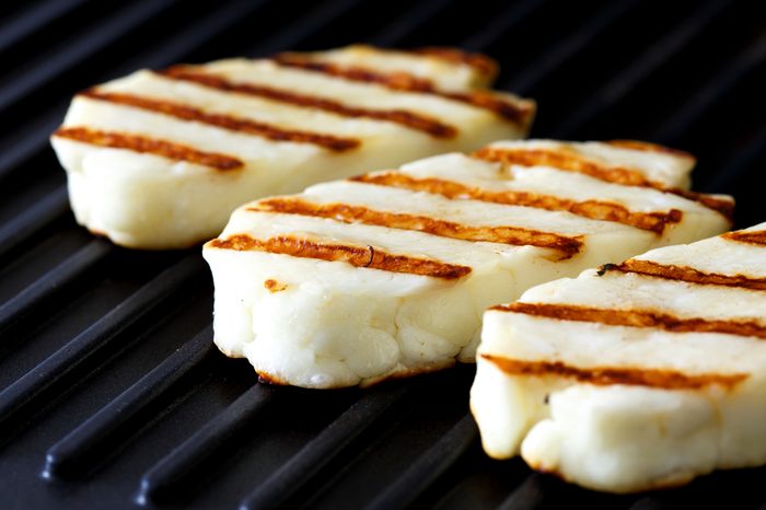 Three grilled slices of halloumi cheese on grill in perspective. With grill marks.