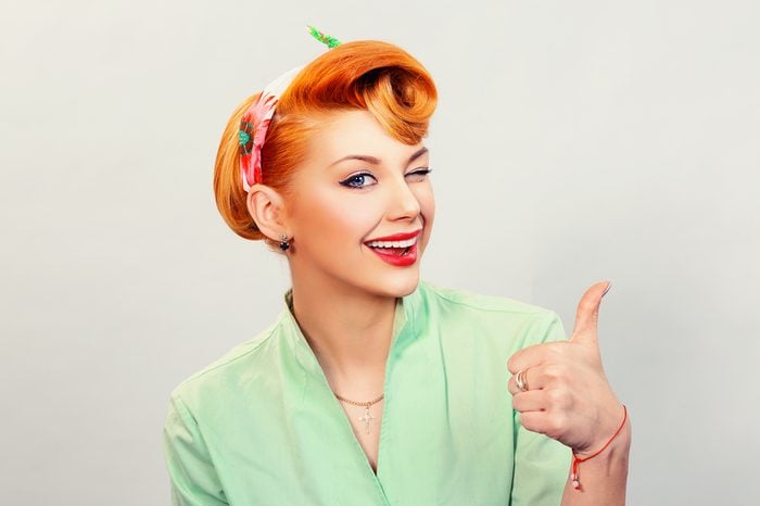 Closeup red head young woman pretty pinup girl green button shirt giving thumbs up sign gesture looking at you camera isolated white background retro vintage 50's style. Human emotions body language
