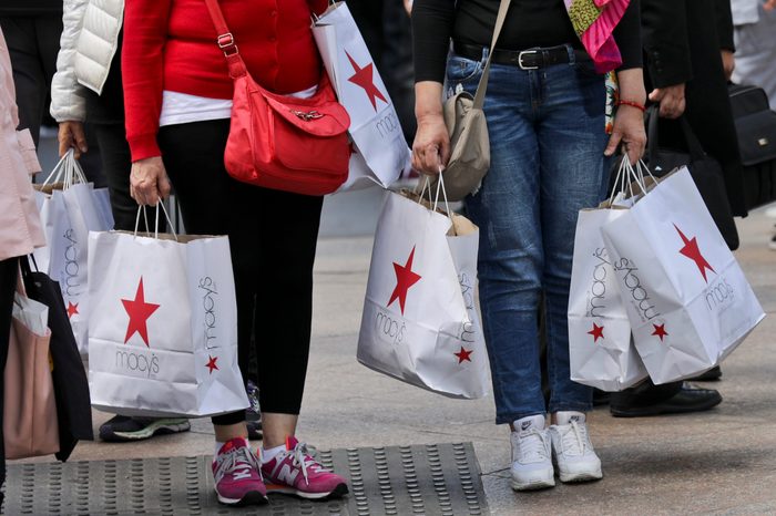 Shoppers holding bags from Macy's wait to cross an intersection in New York.