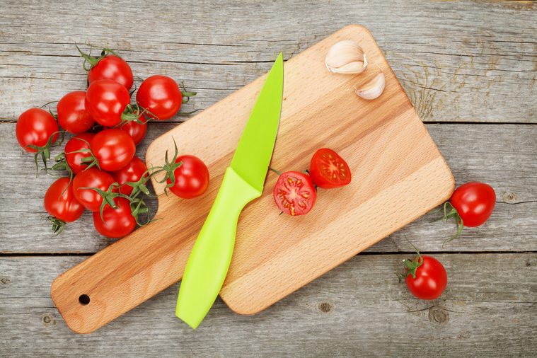 Cherry tomatoes with knife on cutting board over wooden table background