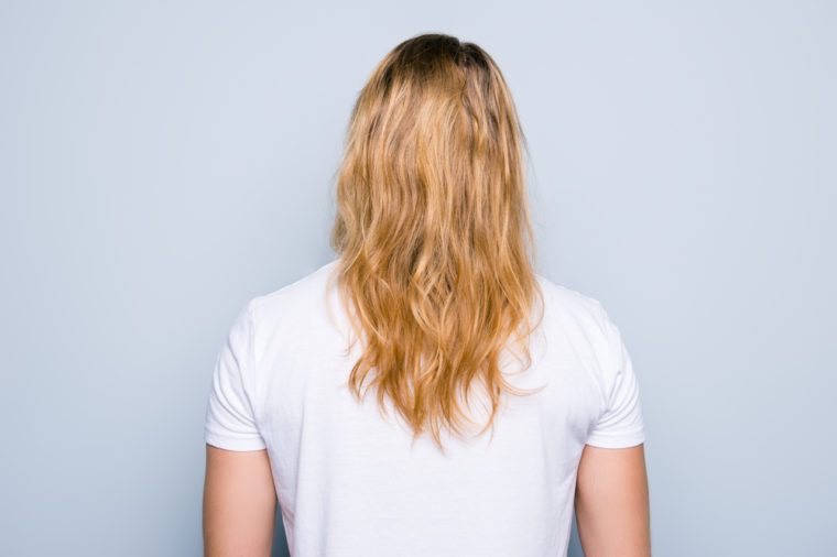 Back view portrait of young man clothed in white tshirt, he has perfect, shiny blonde long healthy hair, isolated on grey background