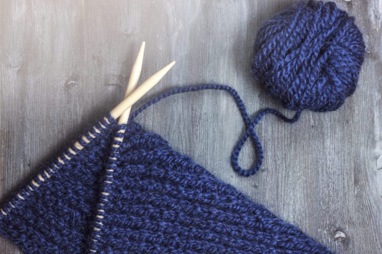 Knitting with wooden knitting needles and blue wool yarn ball on wooden background. Top view or flatlay, surface