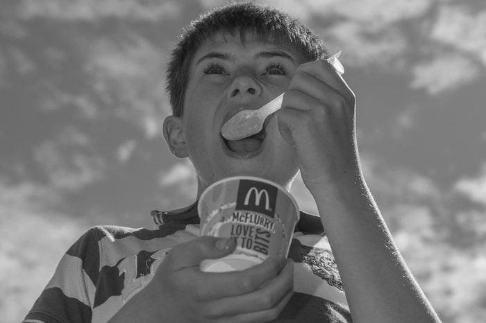 A 12 year old boy eating a mcdonalds Mcflurry ice cream outdoors in the uk