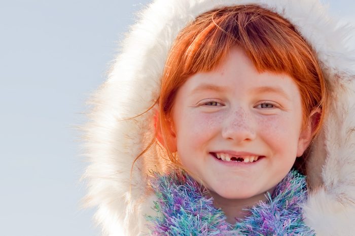 six year-old red haired girl with two front teeth missing and wearing Eskimo style fur lined hood