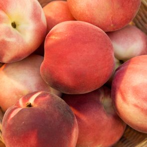 Some peaches  in a basket over a wooden surface seen from above