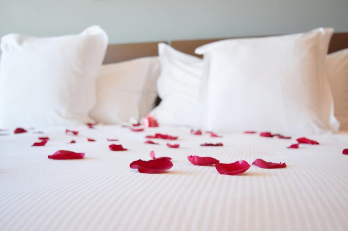 Saint valentine's day, white large bed with the rose petals, red rose petals on the big bed
