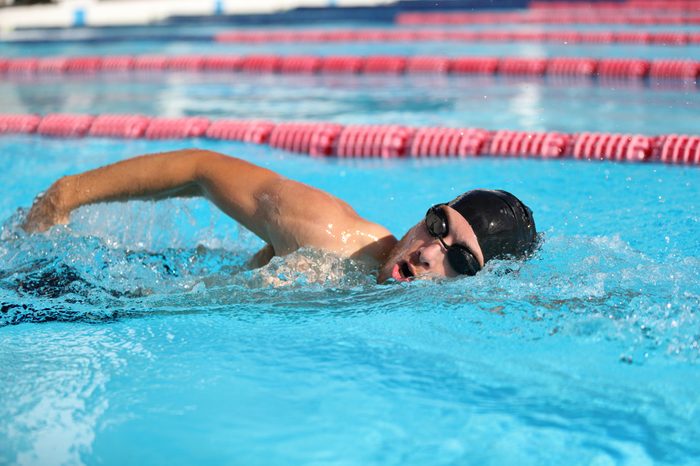 Swim competition swimmer athlete doing crawl stroke in swimming pool. Sports man male swimmer with goggles and cap breathing racing in indoor stadium. Speed exercise workout.