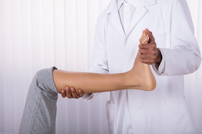 Physiotherapist's Hand Giving Leg Exercise To Female Patient In Clinic