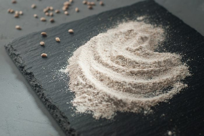 Whole grain flour with wheat grains on dark gray background