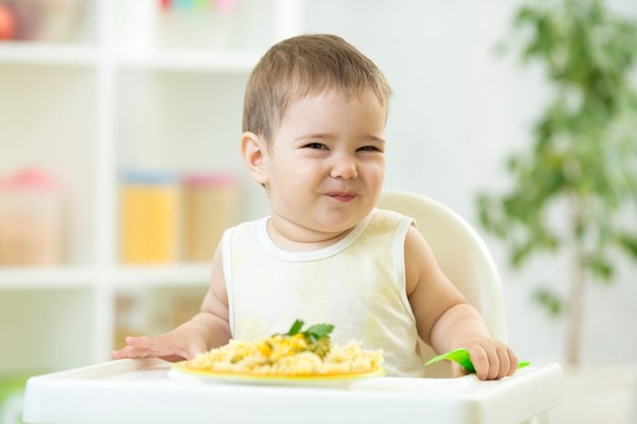 funny baby boy eating healthy food in nursery
