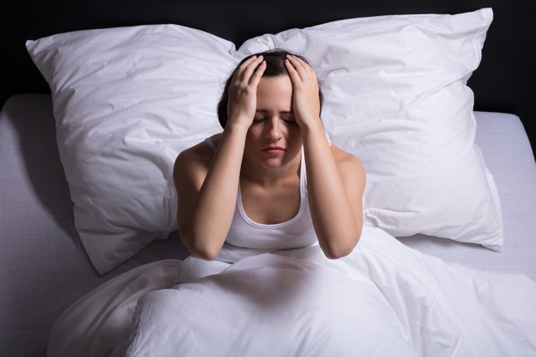 Young Woman Sitting On Bed Suffering From Headache