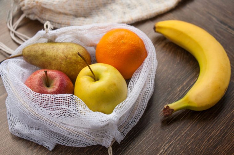 Zero waste, plastic free recycled textile produce bag for carrying fruit (apple, orange, pear and a banana) or vegetables, a wooden surface. Bags are made with a sewing machine out of old curtains.
