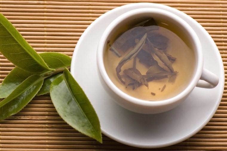 a cup of green tea with fresh leaves on the bamboo tray